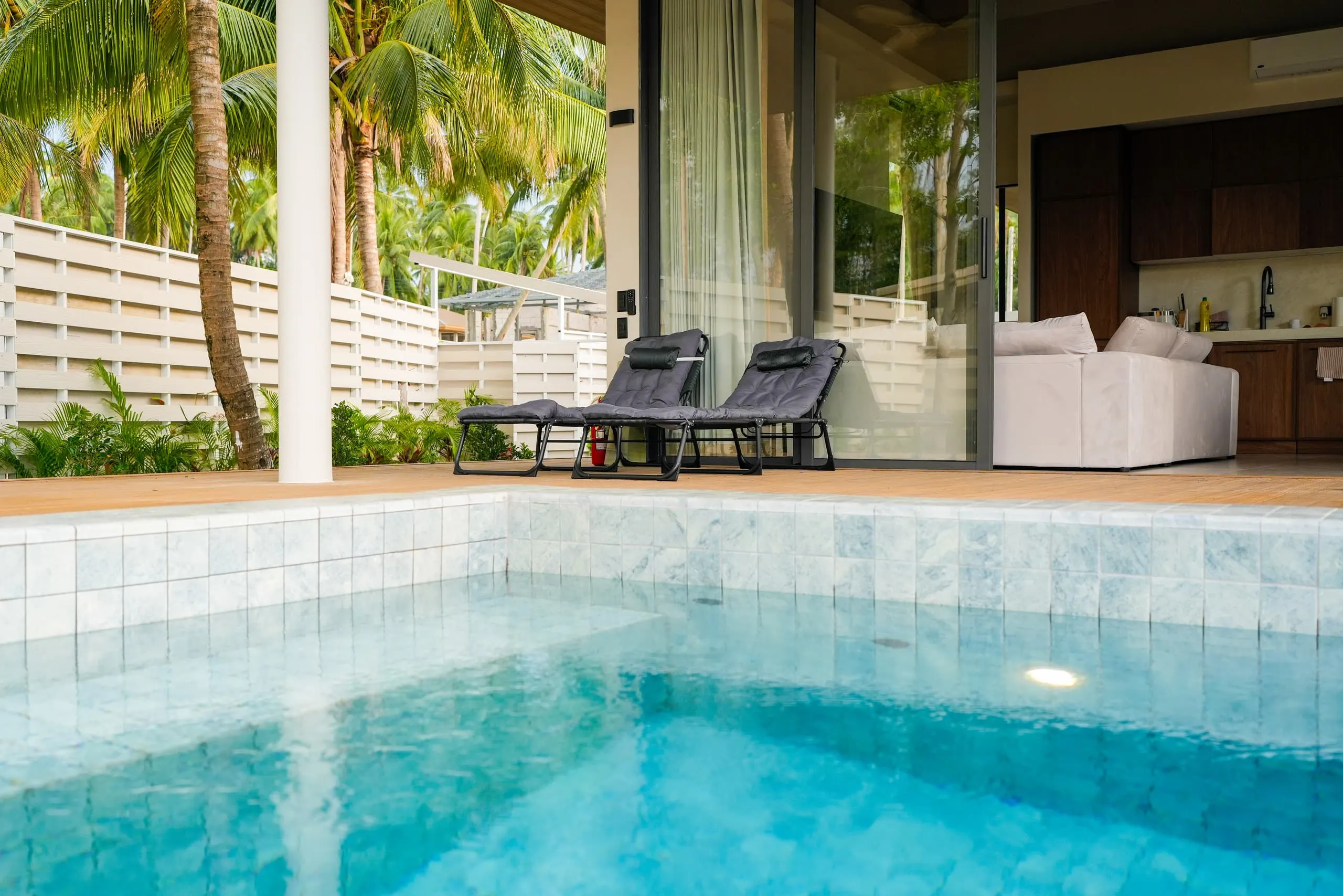 Villa II — pool water and stone edge, sofa visible through the glass
